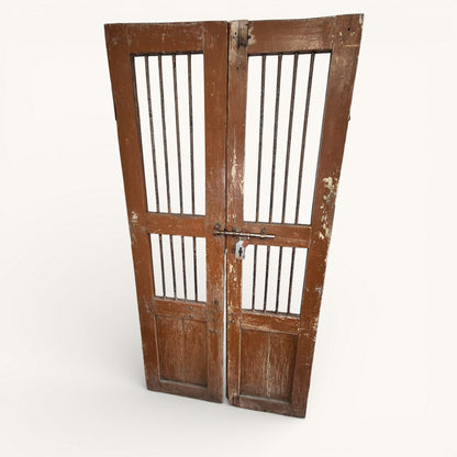 Angled view of antique Indian wooden jali doors showing iron bar panels, original bolt fastening and rustic aged patina.