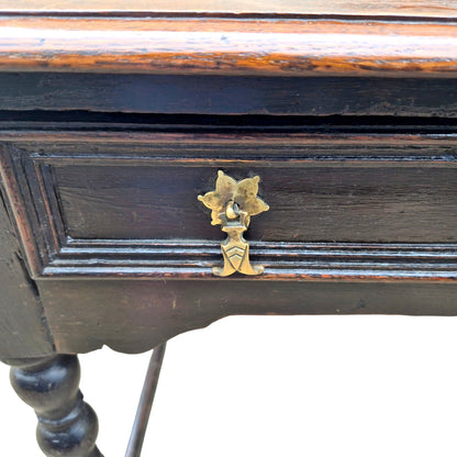 Close-up of antique oak side table drawer with decorative brass handles.