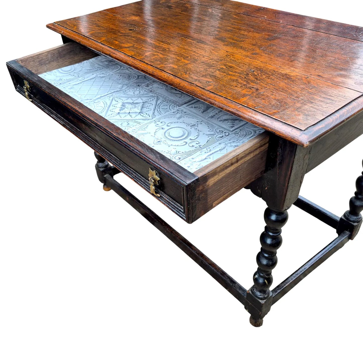 Close-up of antique oak side table drawer with decorative brass handles and aged plank top surface.