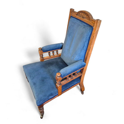 Antique Victorian oak nursing armchair with carved backrest, spindle arms and blue upholstery